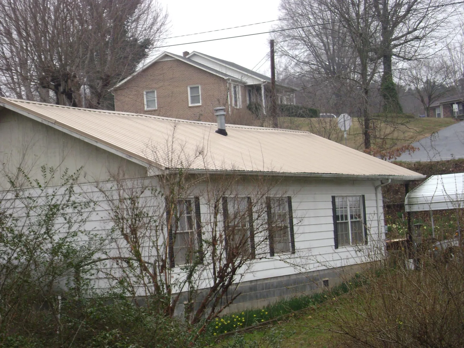 Tan metal roof on a white sided house set into a hillside — Commercial Roofing by Roofing Brothers in New London